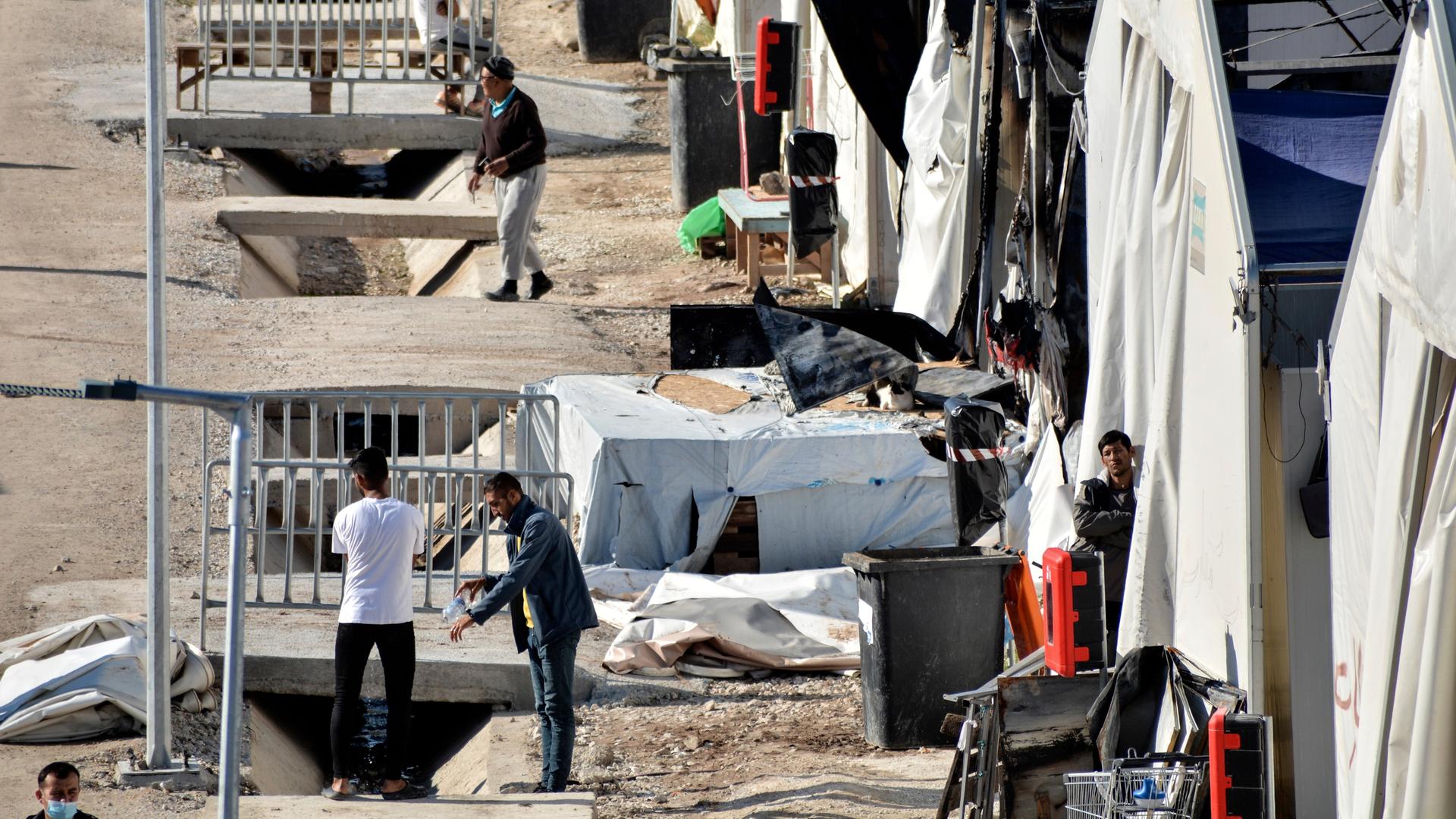 Flüchtlinge in einem Lager auf der Insel Lesbos stehen oder sitzen vor ihren Unterkünften.