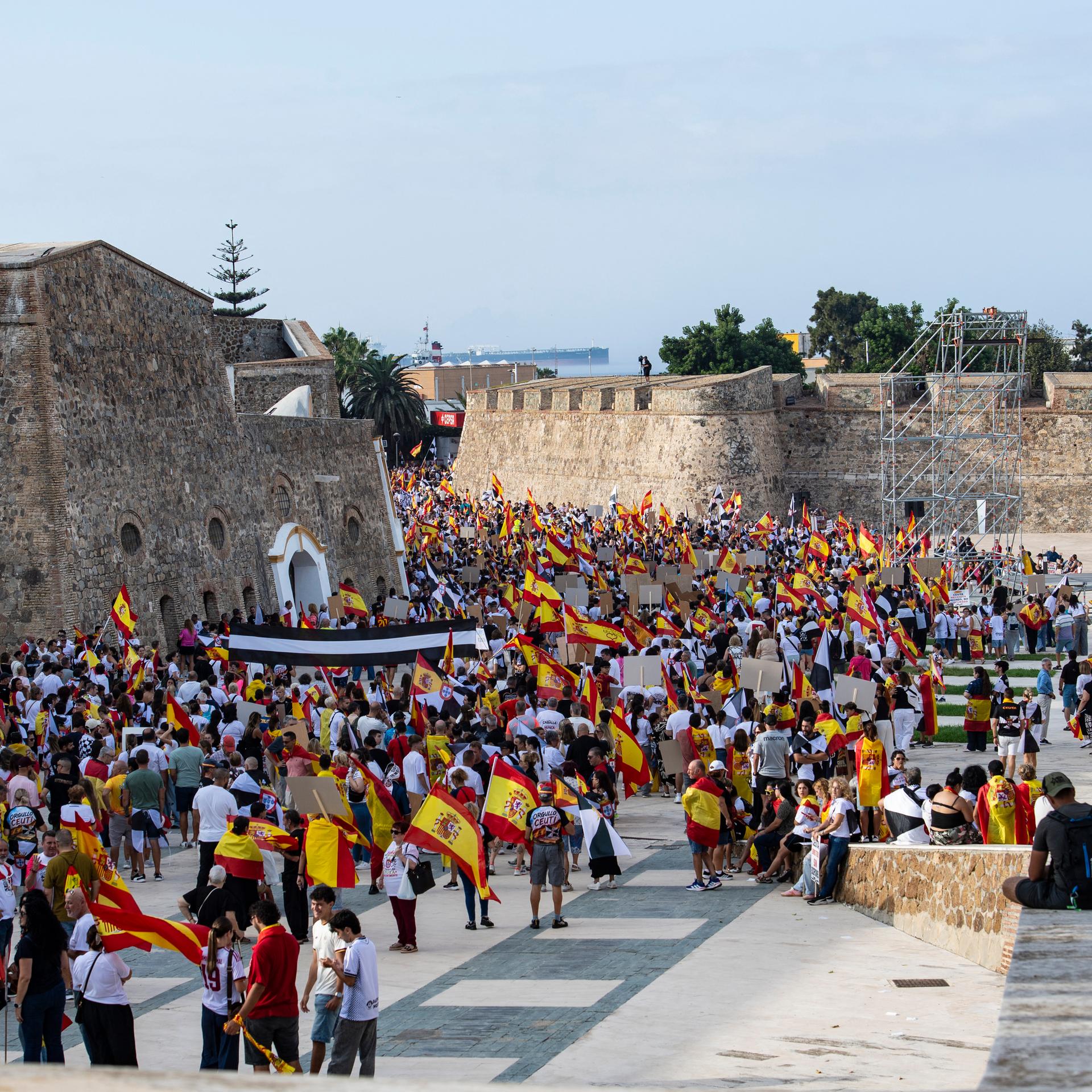 Zwischen alten Burgmauern haben sich viele Menschen versammelt, die spanische Flaggen tragen.
