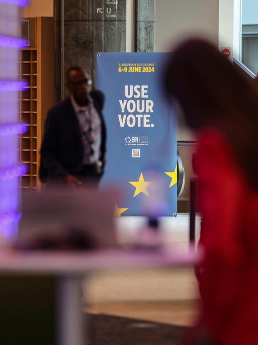 Zwei Menschen im Europäischen Parlament, dahinter ein Plakat mit der Aufschrift "Use Your Vote".
