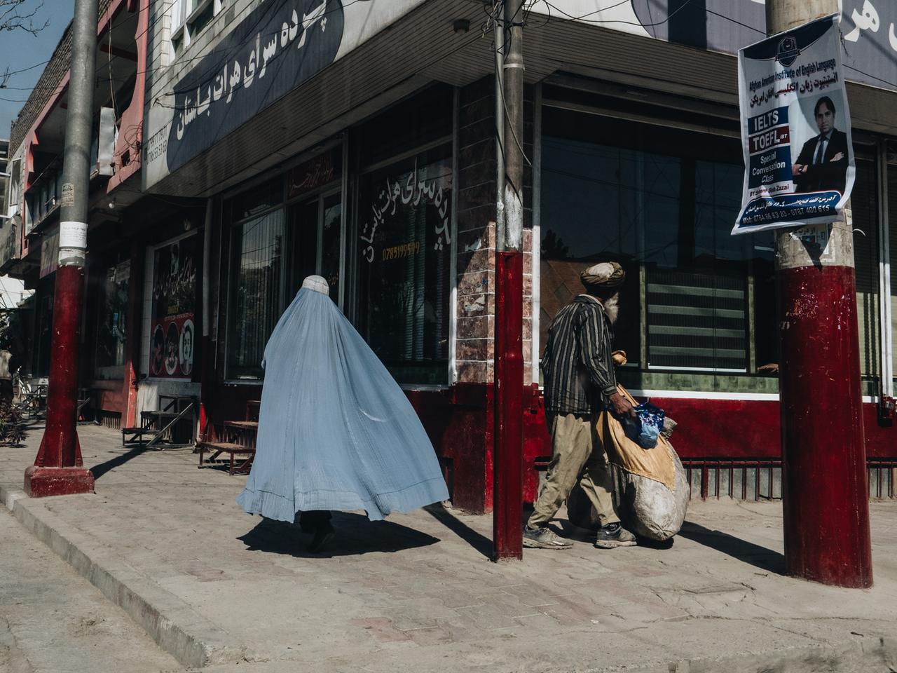 Straßenszene in Kabul: Eine vollverschleierte Frau und ein Mann gehen die Straße entlang.