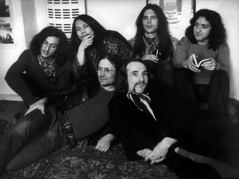 Sechs schwarz gekleidete Musiker der Band The Can posieren für ein Gruppenfoto.