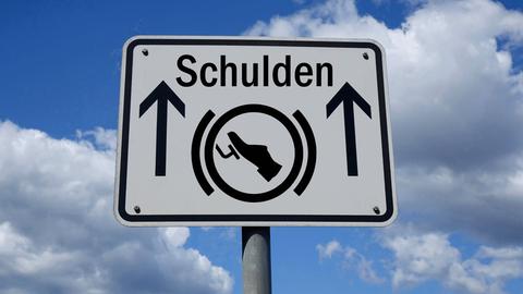 Wegweiser mit dem Wort "Schulden" sowie einer Bremse als Piktogramm. 