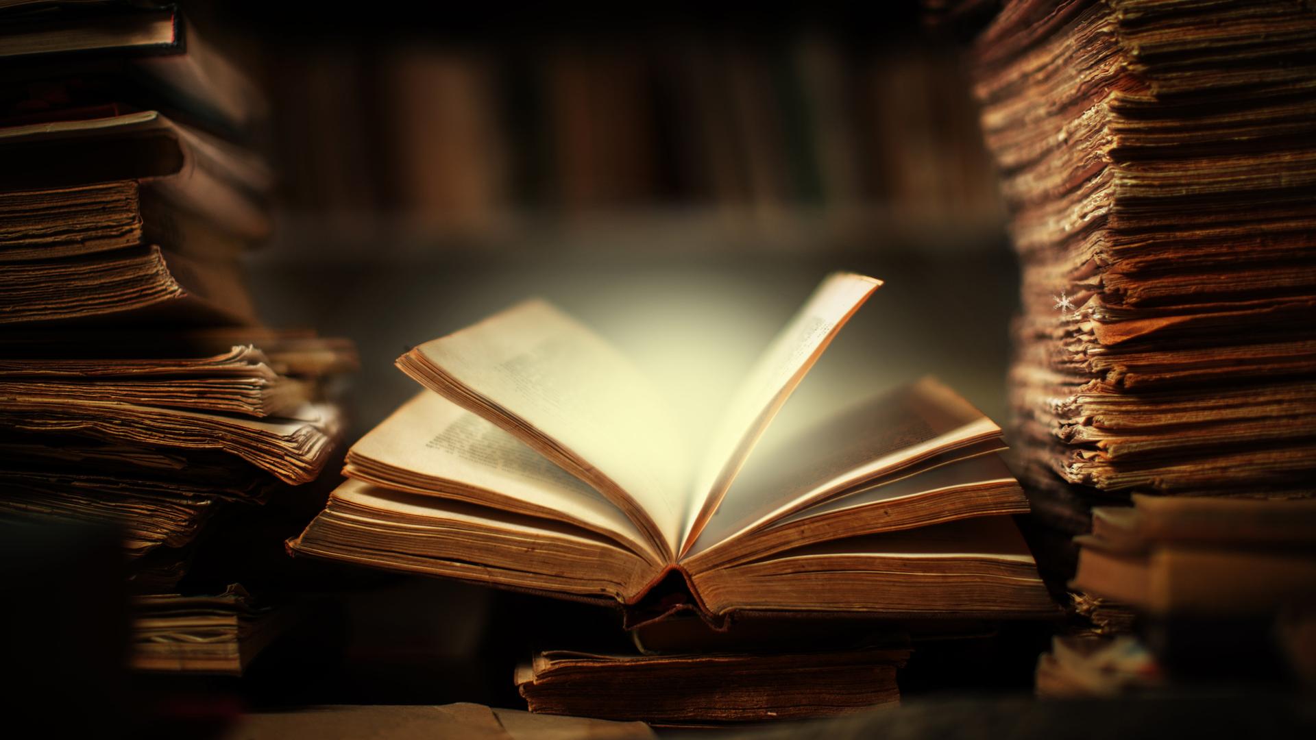 EIn Buch liegt offen auf dem Schreibtisch in der Bibliothek, die Seiten scheinen sich zu bewegen und erhellen die Umgebung durch ein magisches Leuchten