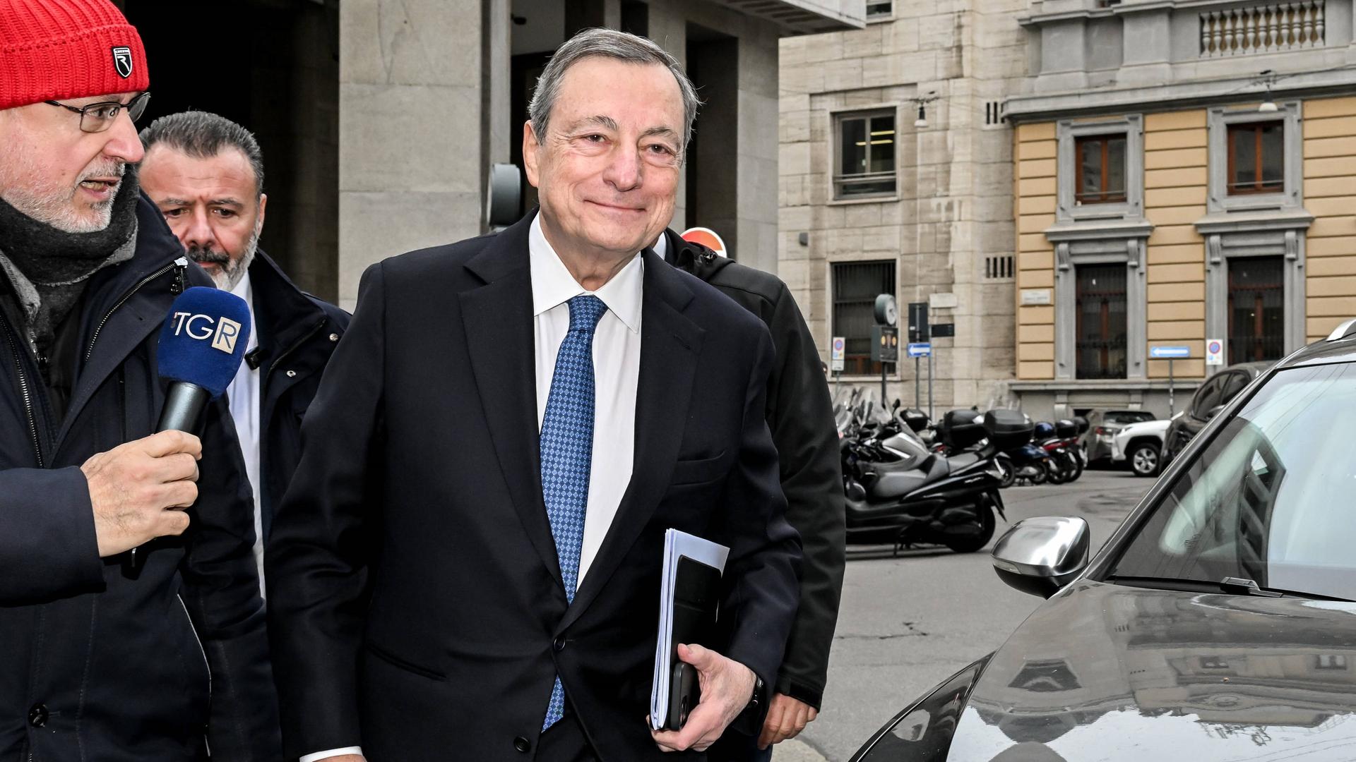 Der frühere italienische Regierungschef und Präsident der Europäischen Zentralbank, Mario Draghi, hält Akten unter dem rechten Arm. Links neben ihm steht ein Journalist, der ihn anspricht.