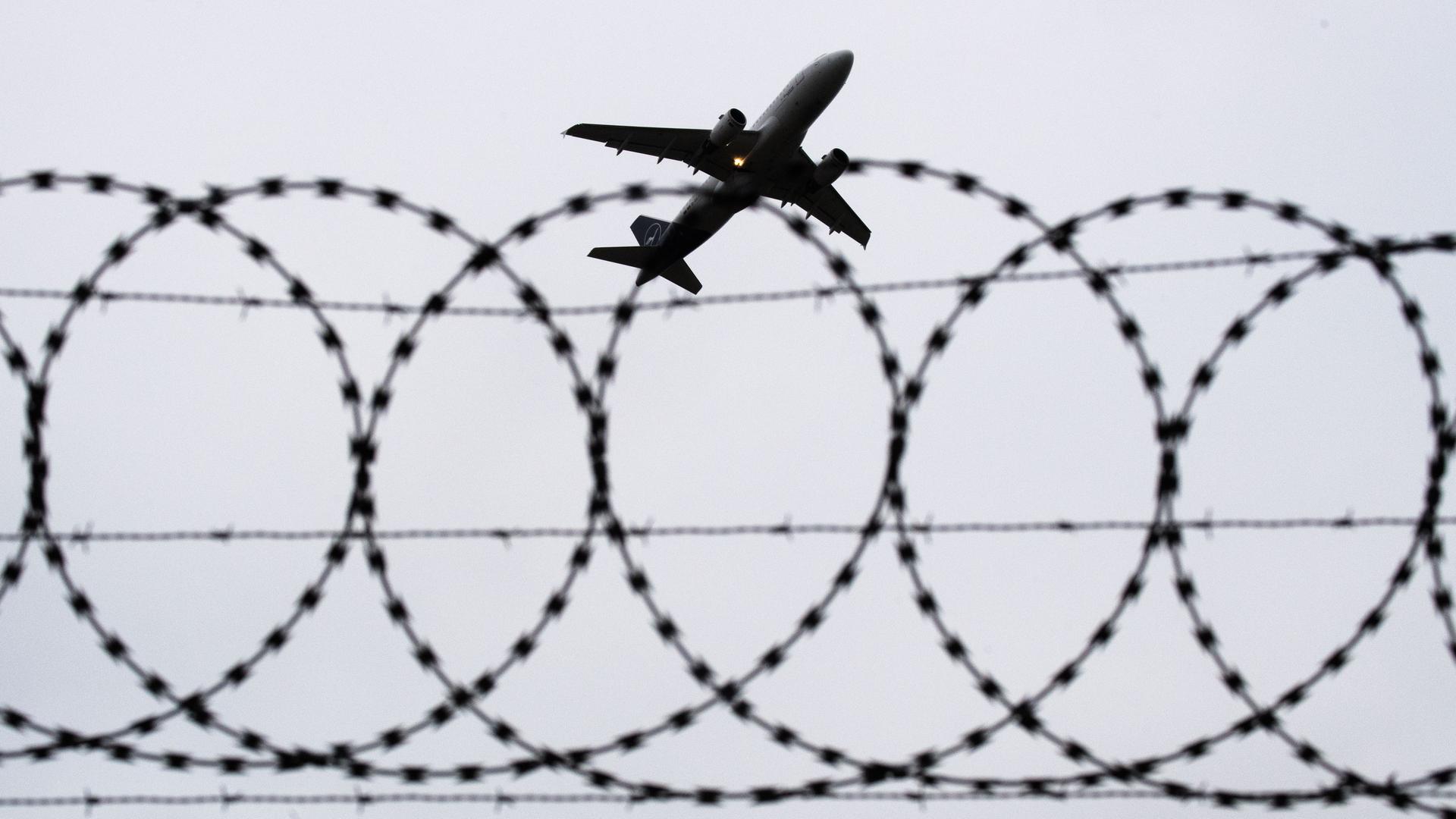 Ein Flugzeug startet, fotografiert durch Stacheldraht am Flughafenzaun.