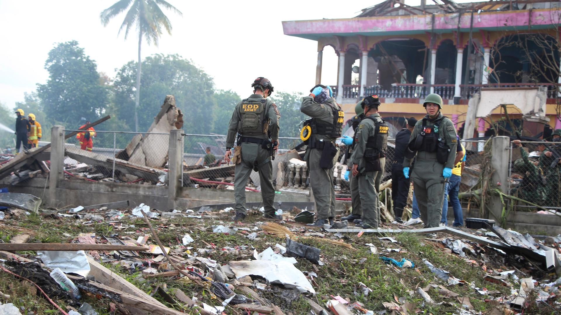 Einsatzkräfte des Kampfmittelräumdienstes stehen vor einem zerstörten Gebäude. Überall liegen Trümmer auf dem Boden.