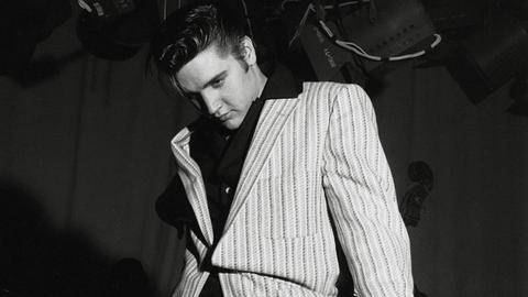 Schwarz-Weiß-Aufnahme von Elvis Presley, der lässig-lasziv an seiner Gitarre lehnt