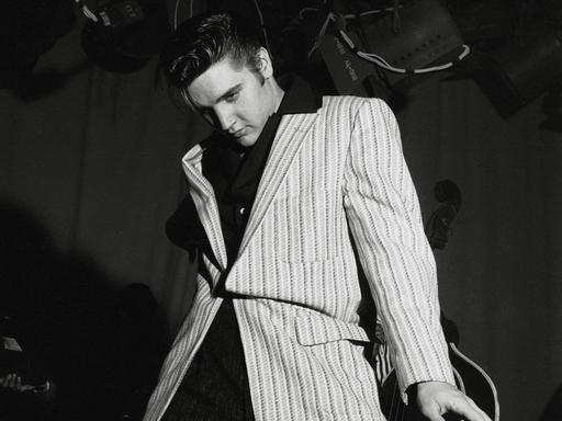 Schwarz-Weiß-Aufnahme von Elvis Presley, der lässig-lasziv an seiner Gitarre lehnt