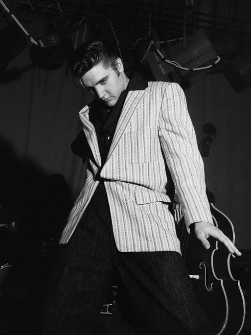 Schwarz-Weiß-Aufnahme von Elvis Presley, der lässig-lasziv an seiner Gitarre lehnt
