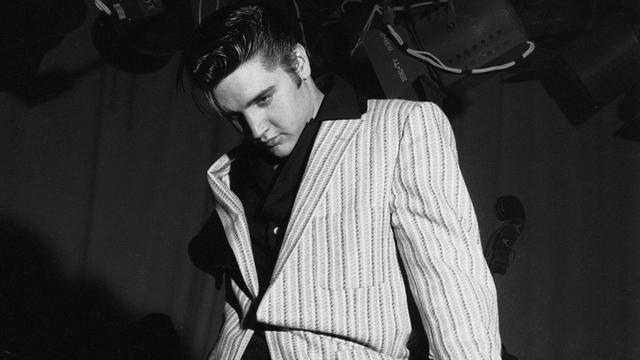 Schwarz-Weiß-Aufnahme von Elvis Presley, der lässig-lasziv an seiner Gitarre lehnt