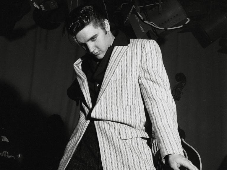 Schwarz-Weiß-Aufnahme von Elvis Presley, der lässig-lasziv an seiner Gitarre lehnt