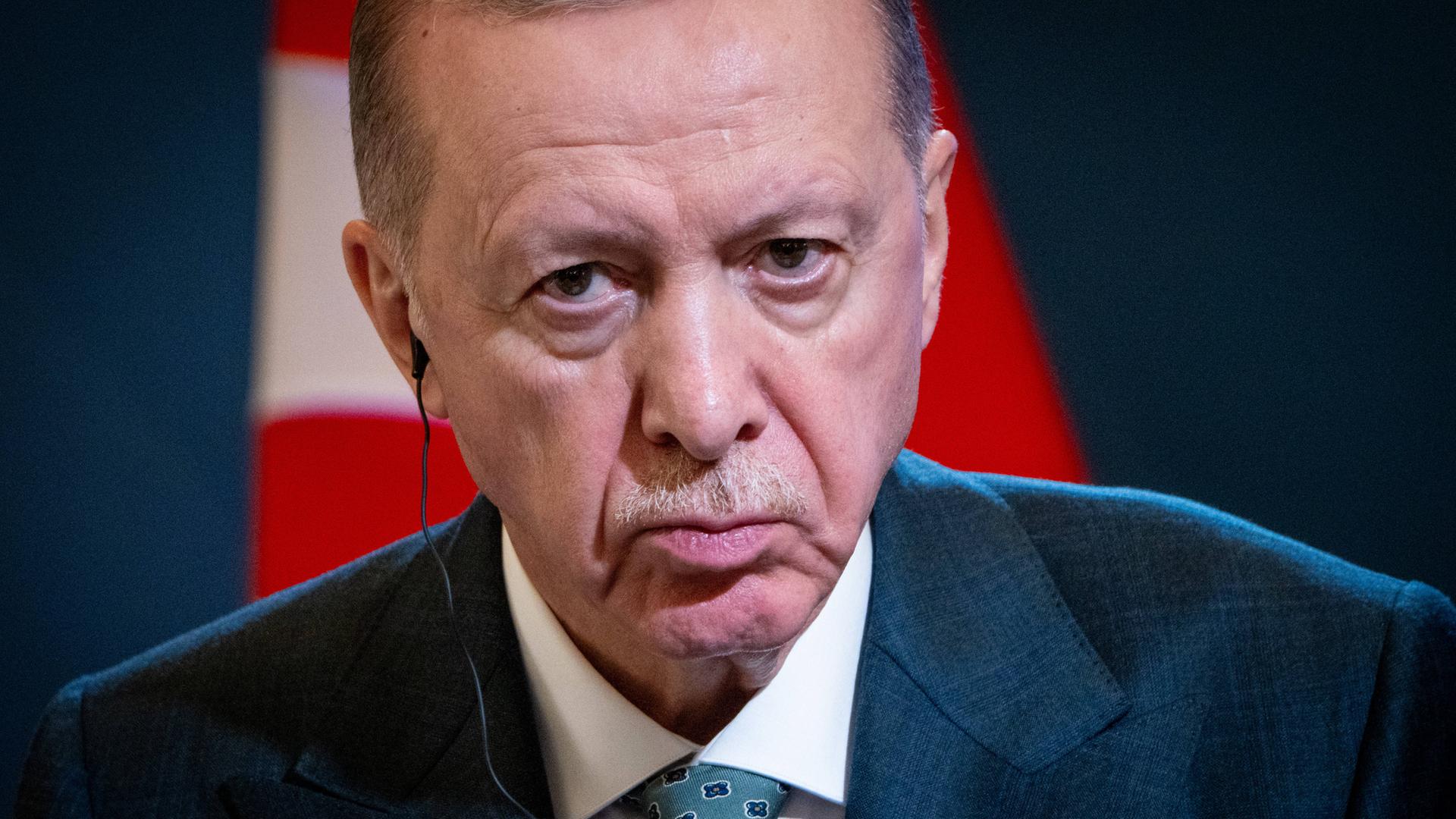 Porträt des türkischen Präsodenten Erdogan, der grimmig in die Kamera guckt. Im Hintergrund sind Teile der türkischen Flagge zu erkennen.