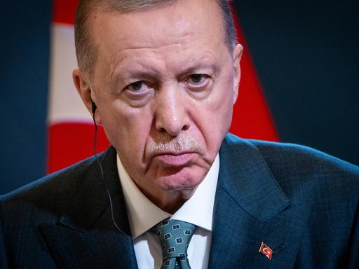 Porträt des türkischen Präsodenten Erdogan, der grimmig in die Kamera guckt. Im Hintergrund sind Teile der türkischen Flagge zu erkennen.