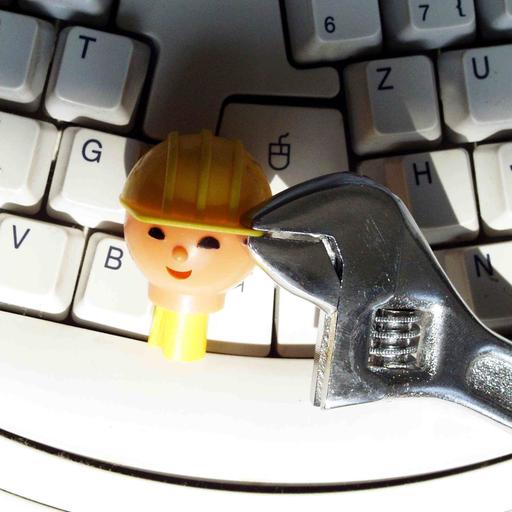 Kopf einer Playmobil-Bauarbeiter-Figur wird auf einer Tastatur mit einer Zange festgehalten