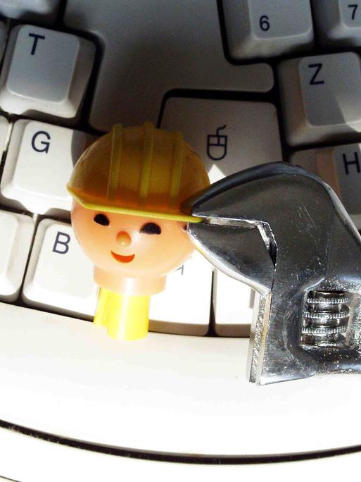Kopf einer Playmobil-Bauarbeiter-Figur wird auf einer Tastatur mit einer Zange festgehalten