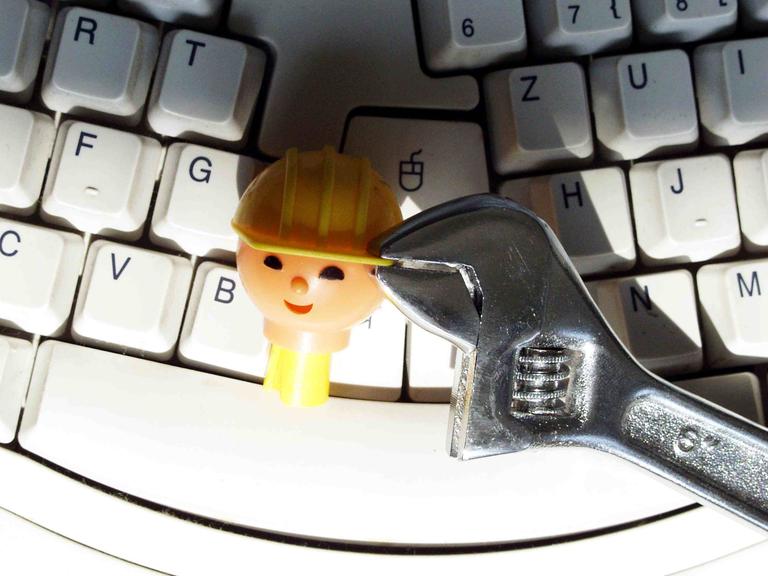 Kopf einer Playmobil-Bauarbeiter-Figur wird auf einer Tastatur mit einer Zange festgehalten Kopf einer Playmobil-Bauarbeiter-Figur wird auf einer Tastatur mit einer Zange festgehalten