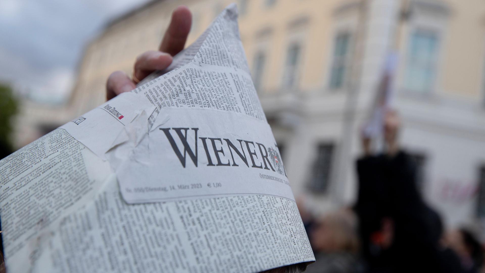 Zu sehen ist eine Seite der "Wiener Zeitung", in der Hand eines Demonstranten.