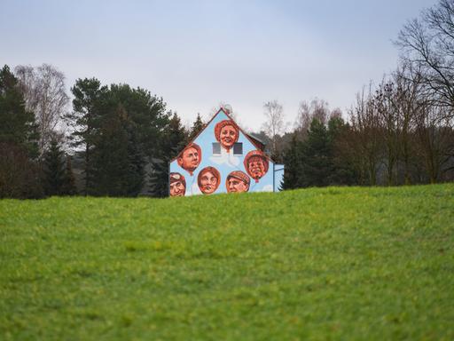 Auf die blaue Fassade eines Mehrfamilienhauses in Fresdorf in Brandenburg, einem ehemaligen Wohnblock aus DDR-Zeiten, sind Gesichter aufgemalt. 