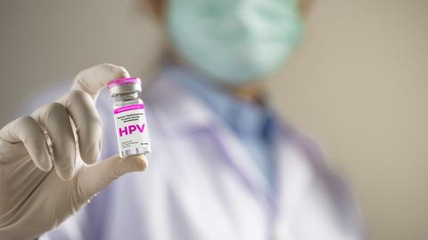 Eine nicht zu erkennende Person hält einen Impfstoff mit der Aufschrift HPV in der Hand und zeigt sie Richtung Kamera