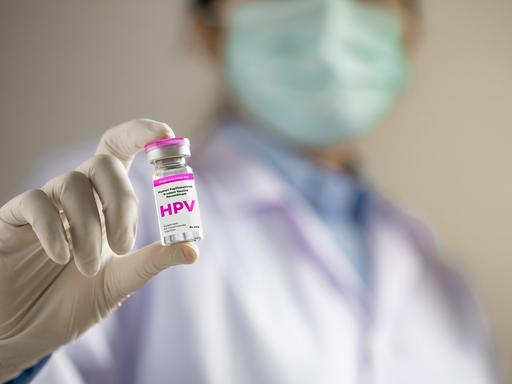 Eine nicht zu erkennende Person hält einen Impfstoff mit der Aufschrift HPV in der Hand und zeigt sie Richtung Kamera