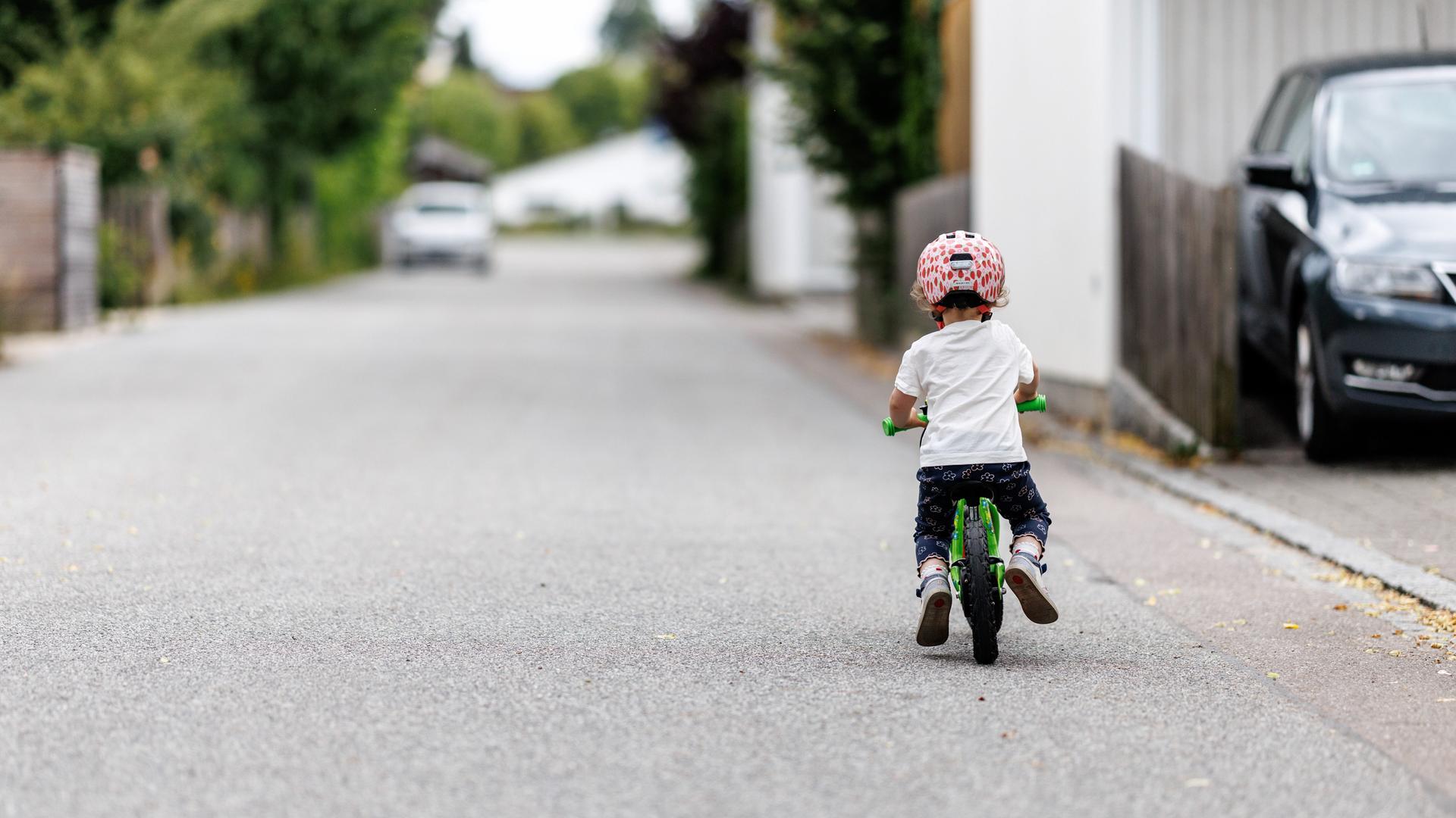 Ein 5-jähriges Mädchen fährt einem Kinderlaufrad zu einem Spielplatz.