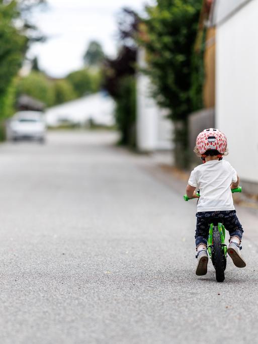 Ein 5-jähriges Mädchen fährt einem Kinderlaufrad zu einem Spielplatz.