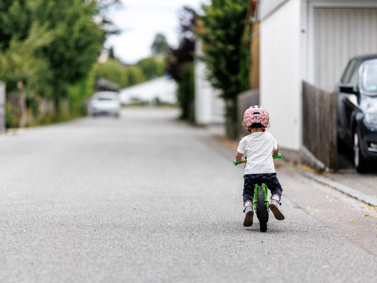Ein 5-jähriges Mädchen fährt einem Kinderlaufrad zu einem Spielplatz.