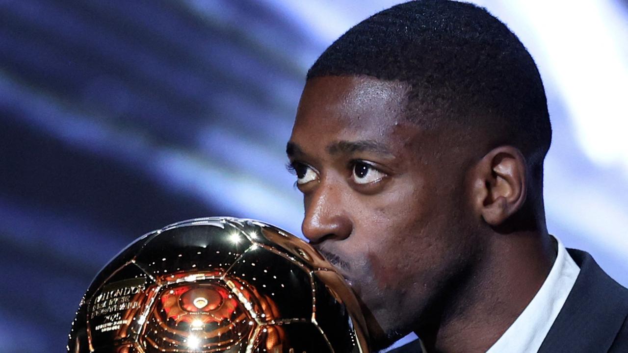 Das Bild zeigt den französischen Profifußballer Ousmane Dembélé, der in Paris mit dem Ballon d'Or ausgezeichnet wurde. Er küsst die Trophäe.