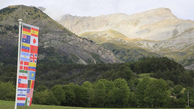 Blick auf die französischen Alpen bei Le Vernet im Sonnenschein, davor eine Fahne mit verschiedenen Flaggen, die an die Opfer des Pilotensuizids vor zehn Jahren erinnern sollen.