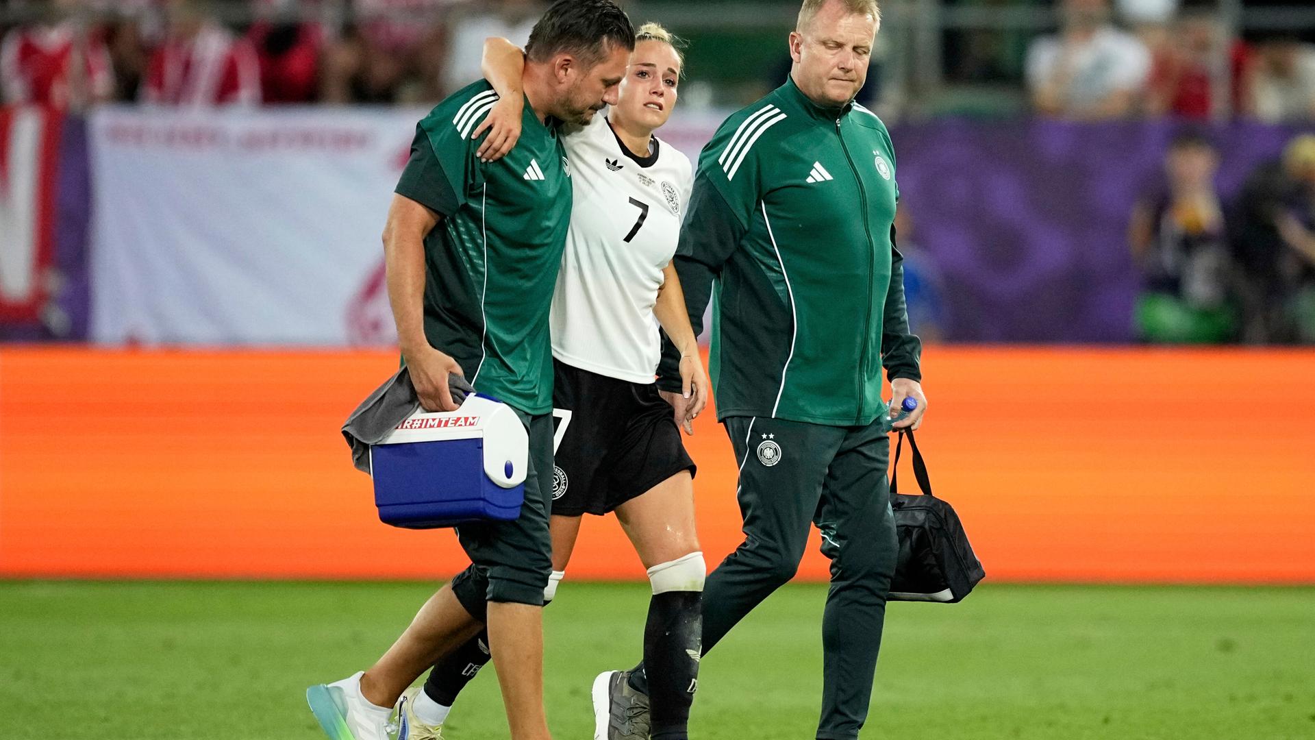 Giulia Gwinn humpelt beim EM-Auftaktspiel gegen Polen in der Schweiz verletzt vom Platz. Sie wird von zwei Betreuern gestützt. 