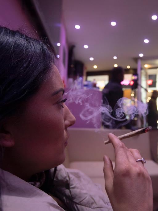 Eine Frau sitz in Amsterdam in einem Coffeeshop und raucht einen Joint.