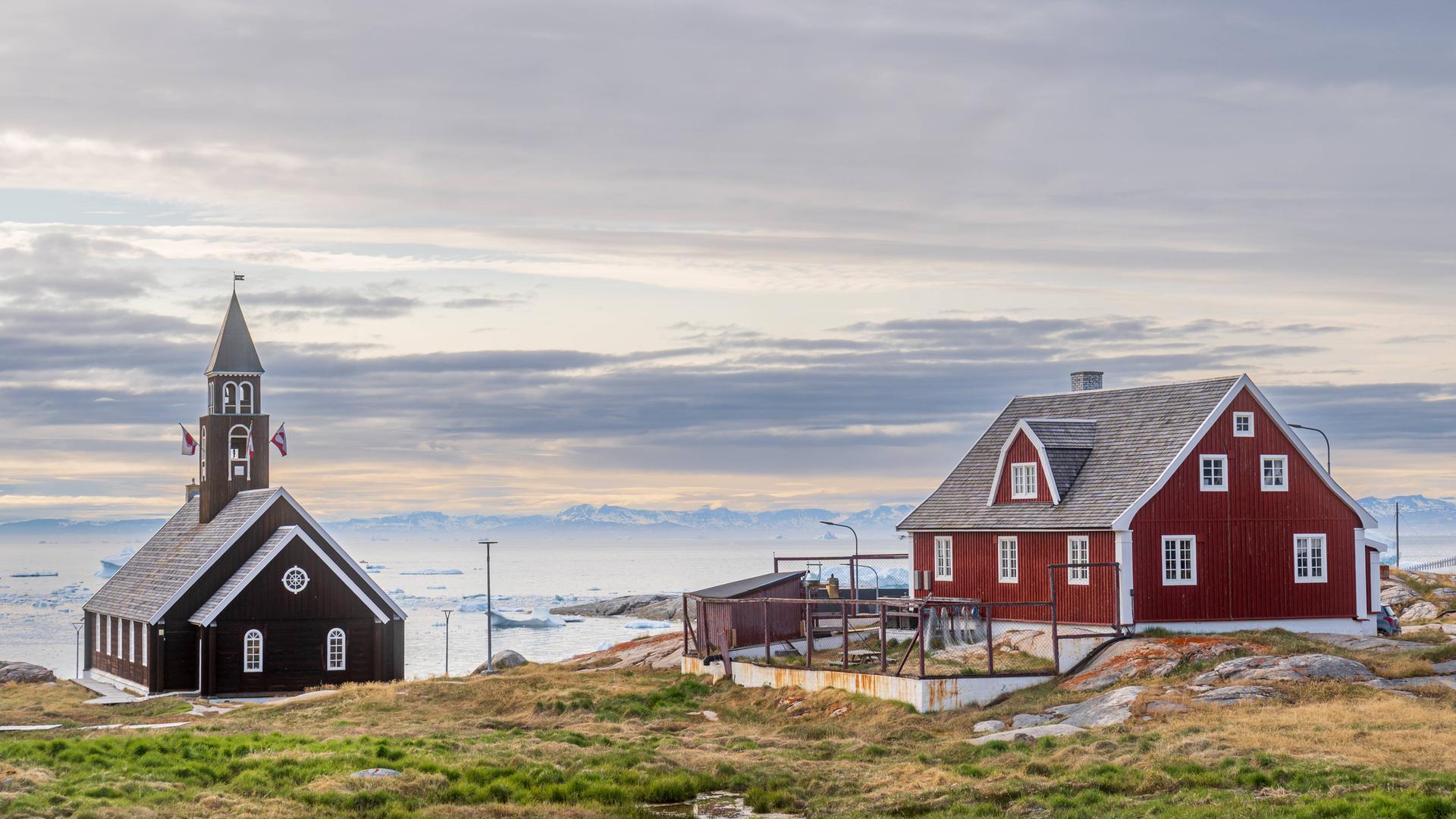Eine hölzerne Kirche und ein traditionelles rotes Wohnhaus am Meer im Ort Ilulissat auf Grönland 