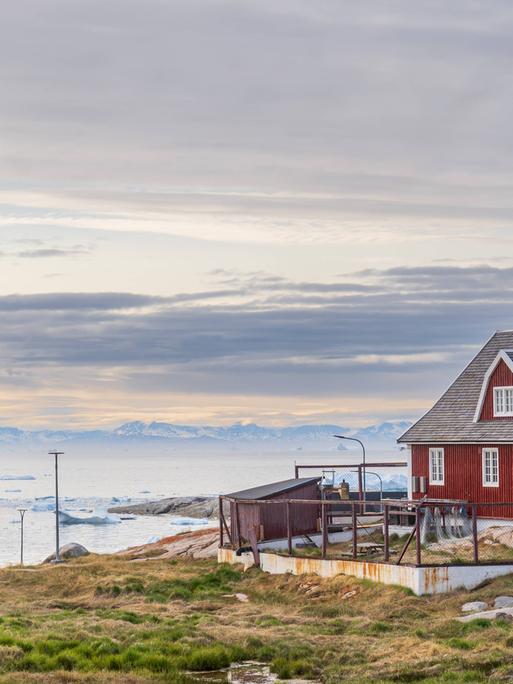 Eine hölzerne Kirche und ein traditionelles rotes Wohnhaus am Meer im Ort Ilulissat auf Grönland 