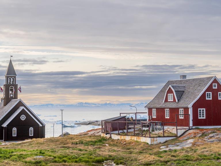 Eine hölzerne Kirche und ein traditionelles rotes Wohnhaus am Meer im Ort Ilulissat auf Grönland 