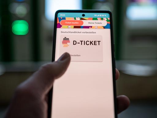 Ein Mann hält ein Mobiltelefon, auf dem das Deutschland-Ticket gekauft werden kann.