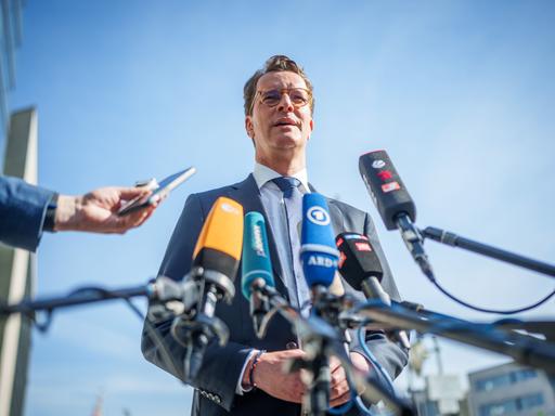 Hendrik Wüst (CDU), Ministerpräsident von Nordrhein-Westfalen, steht vor Mikrofonen im Freien und spricht. 
