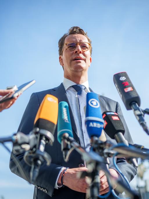 Hendrik Wüst (CDU), Ministerpräsident von Nordrhein-Westfalen, steht vor Mikrofonen im Freien und spricht. 