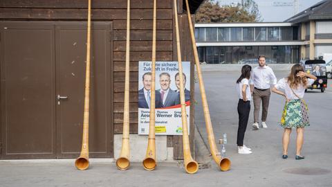 Mehrere Alphörner verdecken ein SVP Wahlplakat, das anläslich eines Parteitages der SVP in Zug an einem Holzhaus hängt.