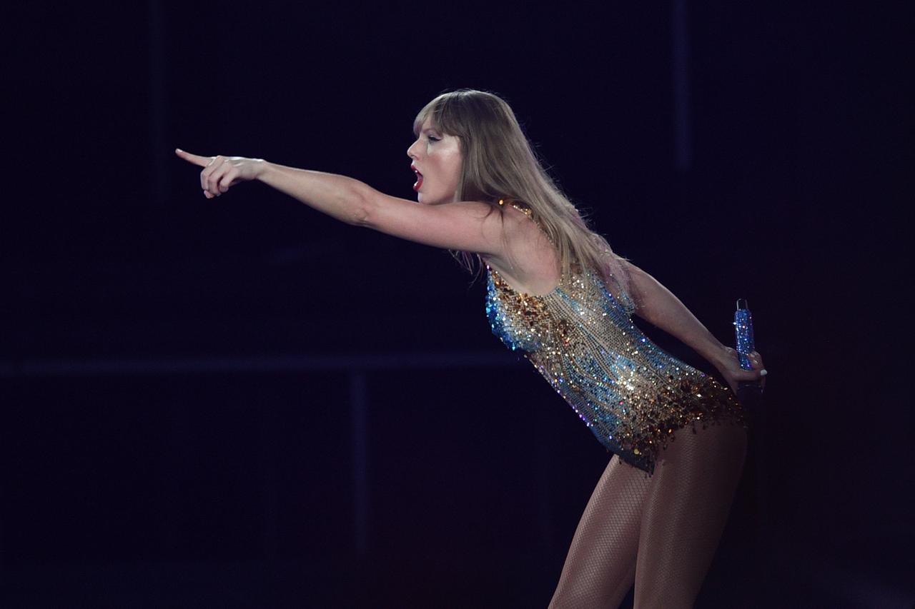 Eine weiße Frau in glitzerndem Bühnenkostüm schaut nach links und zeigt nach links: Es ist die Sängerin Taylor Swift bei einem Auftritt in Sydney im Februar 2024.