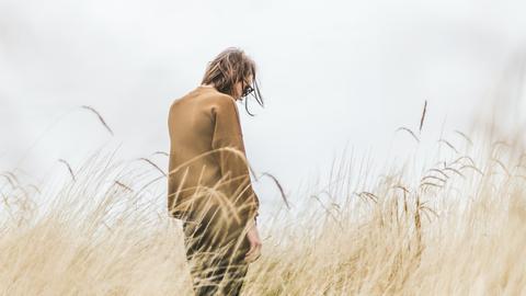 Rückenansicht eines Mannes, der alleine in einem Feld steht.