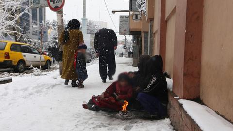 Menschen sitzen vor einem Feuerchen im Schnee auf einer Strasse in Kabul.