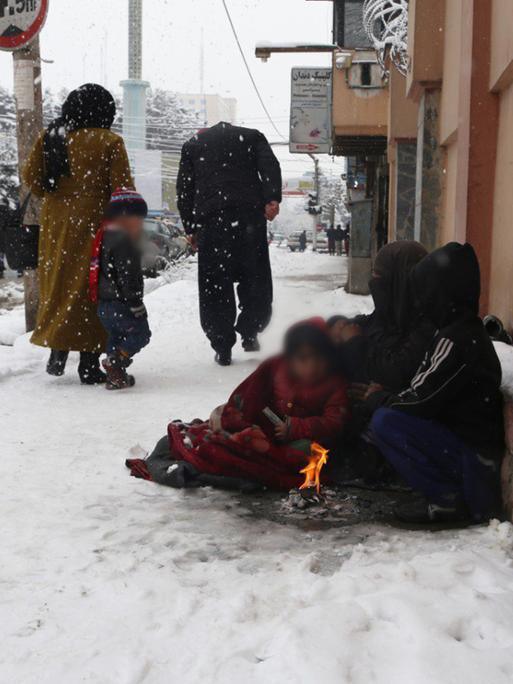 Menschen sitzen vor einem Feuerchen im Schnee auf einer Strasse in Kabul.