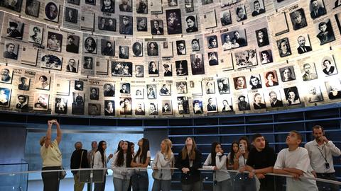 Besucher der Holocaust Gedenkstätte Yad Vashem in Jerusalem. Über ihnen schwebt ein Trichter mit Bildern von ermordeten Juden. 
