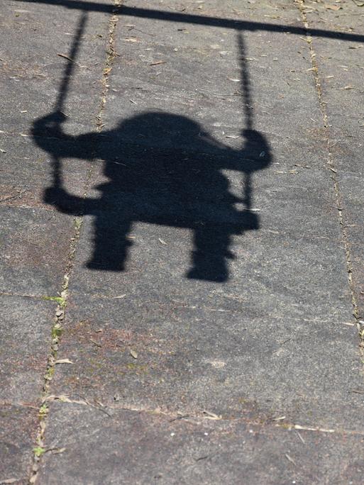 Schatten eines schaukelnden Kindes auf Asphaltboden. Ein Symbolbild für Kinder ohne Geburtsurkunde.