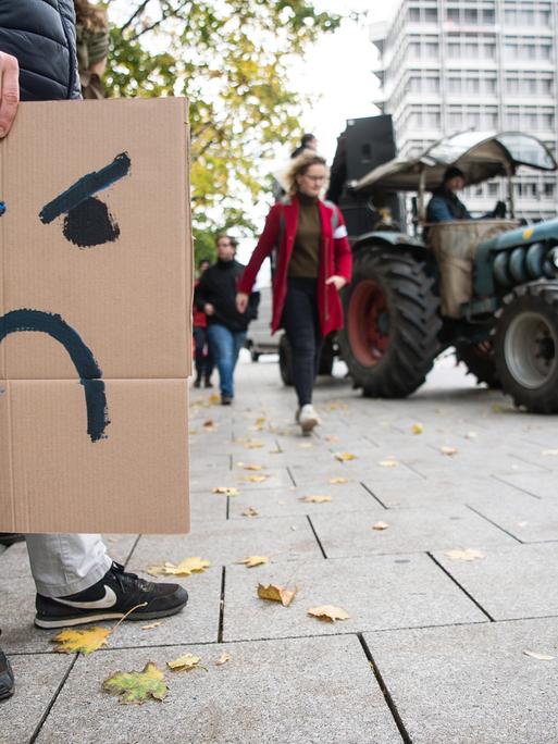 Ein Mann hält während einer Demonstration ein Schild in der Hand, auf dem ein verärgerter Smiley gezeichnet ist. Ein Mann hält während einer Demonstration ein Schild in der Hand, auf dem ein verärgerter Smiley gezeichnet ist.
