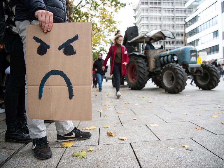 Ein Mann hält während einer Demonstration ein Schild in der Hand, auf dem ein verärgerter Smiley gezeichnet ist. Ein Mann hält während einer Demonstration ein Schild in der Hand, auf dem ein verärgerter Smiley gezeichnet ist.