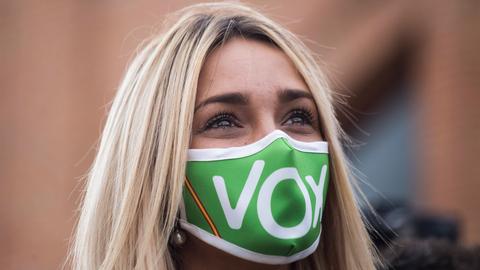 Eine junge blonde Frau trägt eine grüne Maske, auf der mit weißen Buchstaben Vox steht.