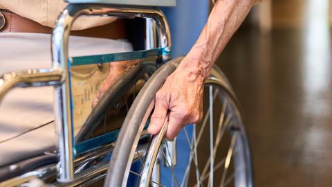Nahaufnahme: Ältere Person hält Rollstuhlrad im Korridor einer Rehabilitationseinrichtung