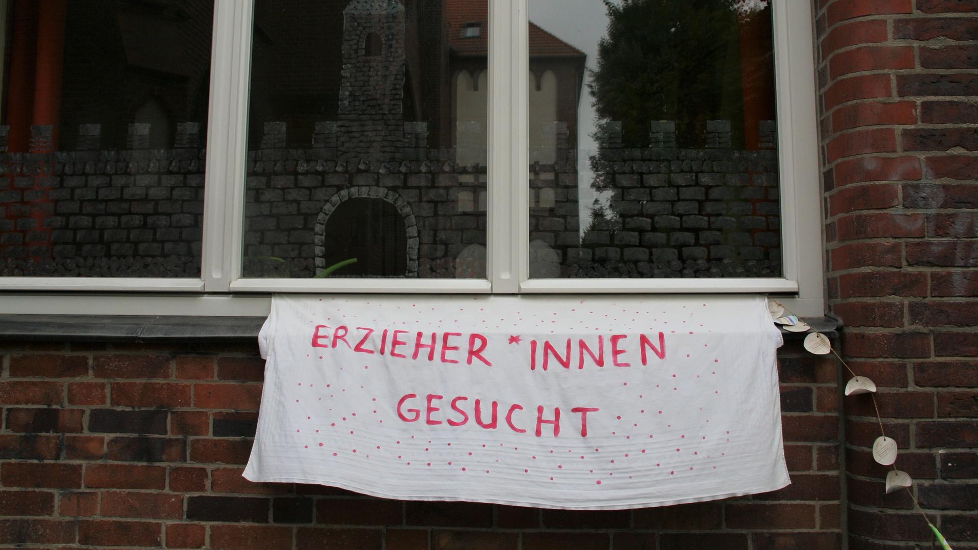 Mit einem Transparent wird an der Außenwand einer Kita in Berlin um Erzieher*innen geworben.