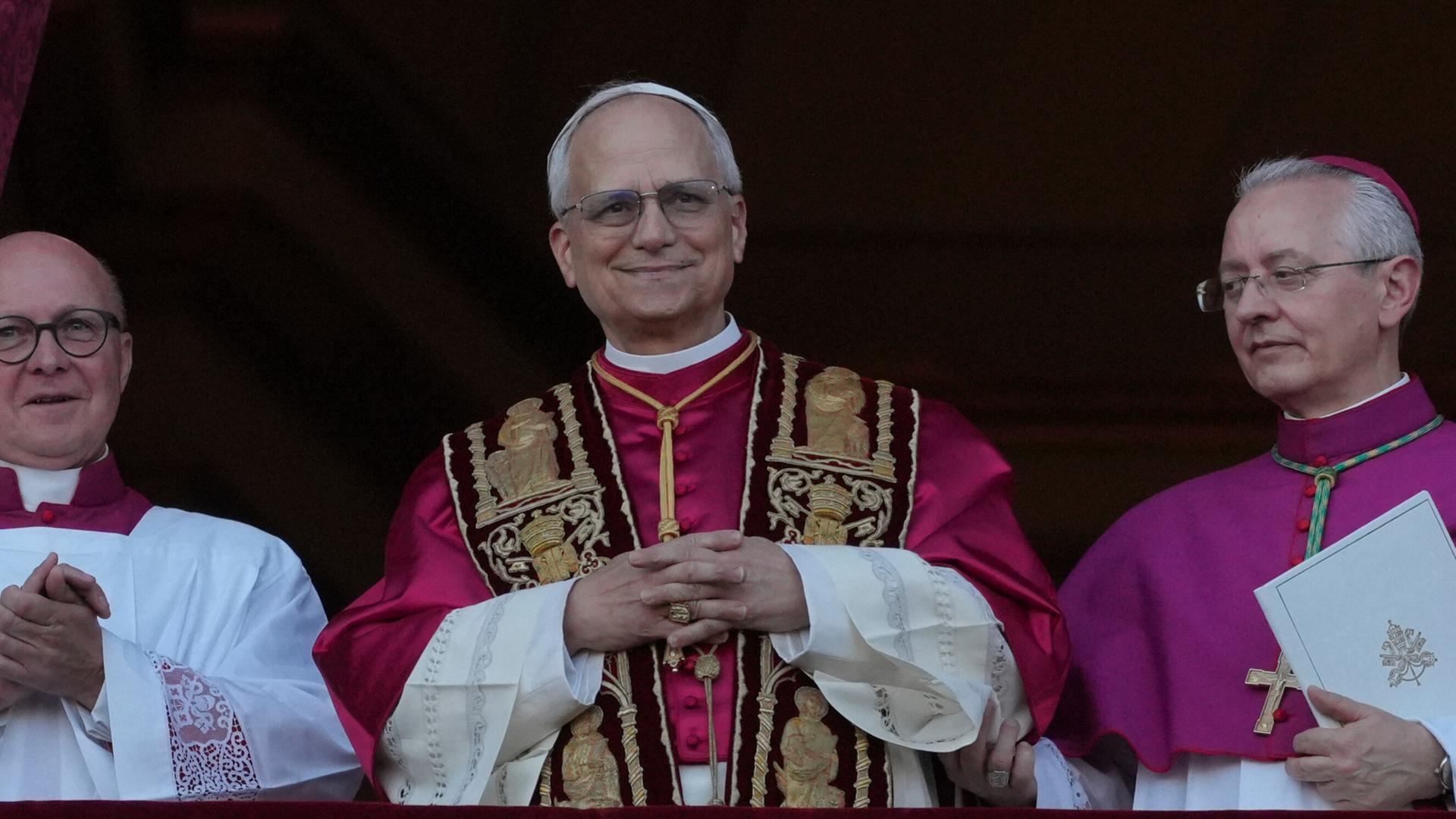 Der neu gewählte Papst, Leo XIV, steht auf dem Balkon des Petersdoms im Vatikan am 8. Mai 2025. Seine Hände sind gefaltet und er hat ein Lächeln auf den Lippen - Er scheint sichtlich glücklich über sein neues Amt.